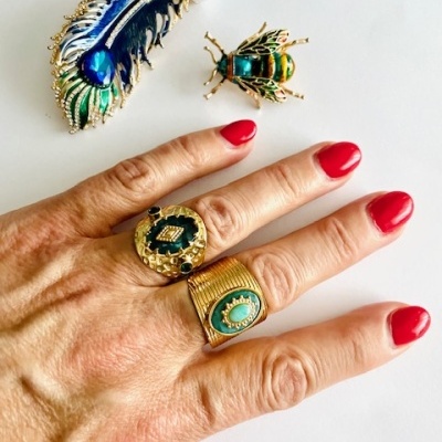 Anel dourado com pedra verde e broches coloridos em mesa branca