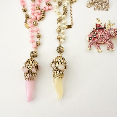 Dois colares com pendentes em forma de presa cor de rosa e amarelo pálido com detalhes dourados e pedras.