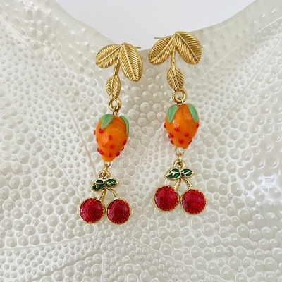 Brincos dourados com morango e cerejas em fundo branco texturizado