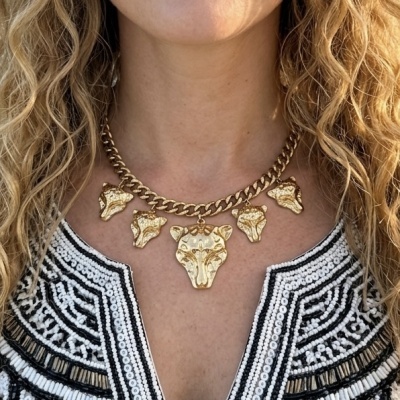 Colar dourado com pendentes de cabeça de leão e blusa branca com padrão preto