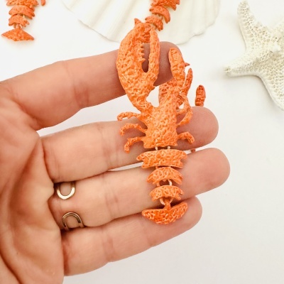 Colar lagosta laranja com textura detalhada segurado por dedos