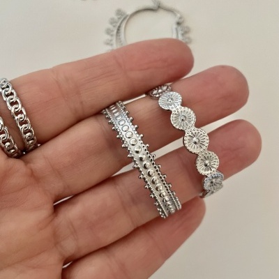 Duas pulseiras prateadas com padrões em relevo seguradas por uma mão frente a fundo branco.