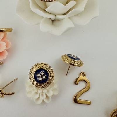 Brincos dourados com detalhes azuis e flores brancas em fundo branco