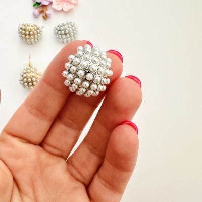 Brinco redondo com pérolas brancas segurado entre dedos com unhas vermelhas