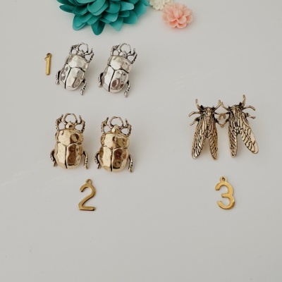Brincos metálicos em forma de insetos com flores decorativas em fundo branco