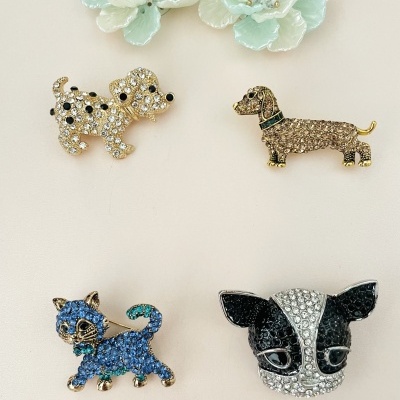 Cinco pins decorativos, dois flores brancas e três cães coloridos com pedras brilhantes.