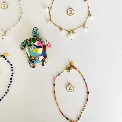 Quatro peças de bijuteria numeradas com contas coloridas, pérolas e tartaruga decorativa sobre fundo branco.