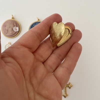 Relicário de coração dourado na mão com outros pendentes no fundo