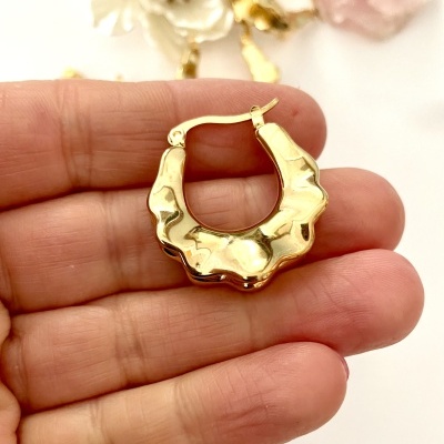 Brinco de argola dourado com textura ondulada na mão