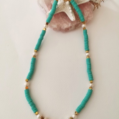 Colar com contas azuis, pérolas e douradas apoiado em conchas sobre fundo branco