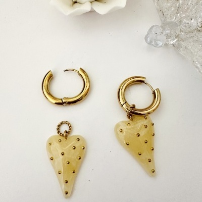 Brincos dourados com corações creme e pontos dourados em fundo branco