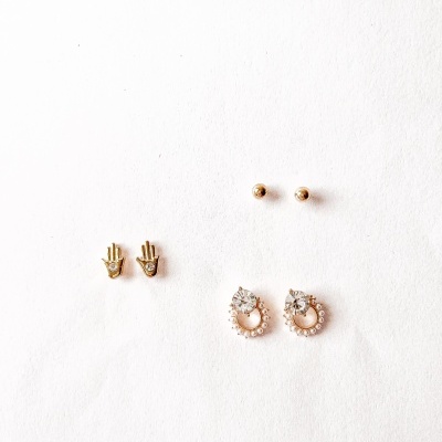 Três pares de brincos dourados e com pedras sobre fundo branco.