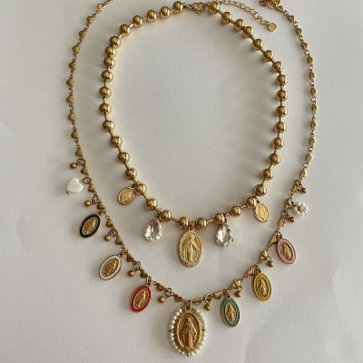 Três colares dourados com medalhas e pedras coloridas sobre fundo branco e flores
