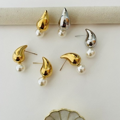 Colares e brincos gota dourados e prateados com pérolas brancas sobre fundo branco com prato decorativo.