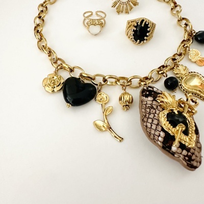 Colar de corrente dourada com vários pendentes e anéis dourados ao fundo