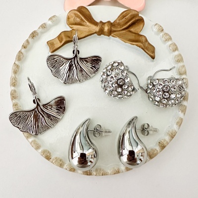 Três pares de brincos em metal prateado sobre prato redondo decorado com laço castanho
