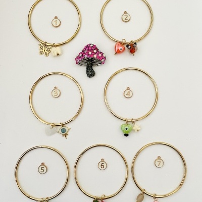 Sete pulseiras douradas com pendentes coloridos numerados de 1 a 7 em fundo branco.