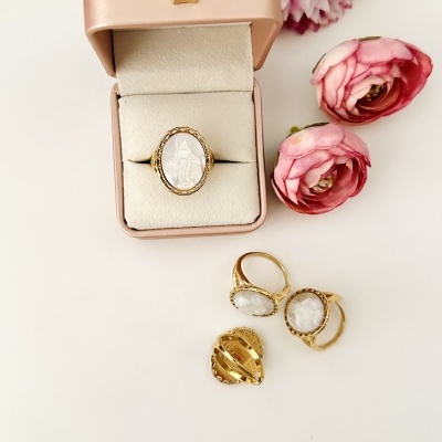 Anel ouro com pedra branca oval na caixa rosa, anéis semelhantes e alfinete dourado com flores rosas