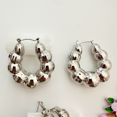 Brincos de argola prateados em formato bolha com fecho de pressão sobre suporte branco