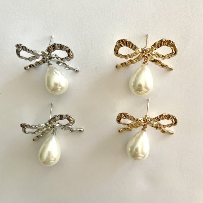 Quatro brincos com laço e pérola pendurada, em metal dourado e prateado, sobre fundo branco.