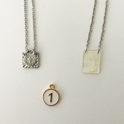Dois colares com pingentes quadrados em metal prateado e um pendente redondo branco com número 1