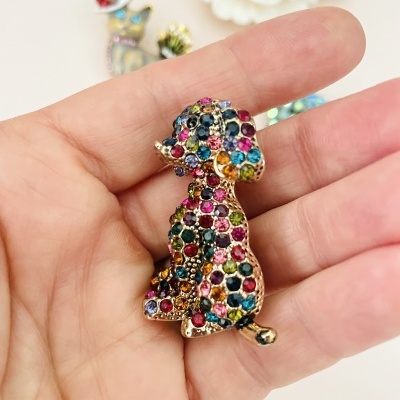 Broche em forma de cão com pedras coloridas e base dourada numa mão.