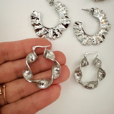 Quatro pares de brincos metálicos prateados com texturas e formas variadas em fundo branco.