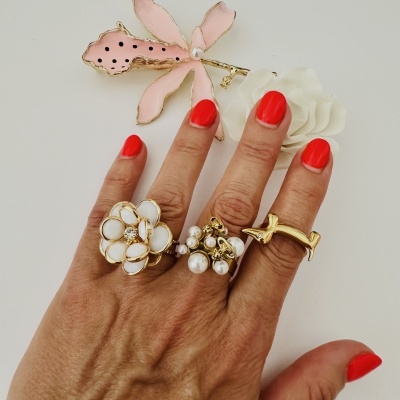 Anel de flor dourado com pétalas brancas e mão com unhas vermelhas