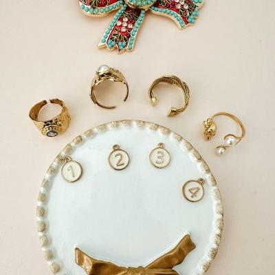 Anéis dourados com pérolas e placa numerada sobre fundo bege