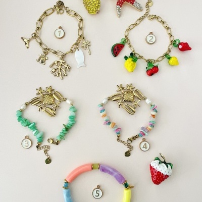 Cinco conjuntos de pulseiras com pendentes de frutas e animais, e broches decorativos coloridos