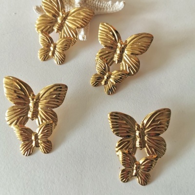 Brincos dourados em forma de borboletas, sobre uma superfície branca com uma estrela-do-mar decorativa