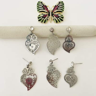 Broche de borboleta colorida e cinco pares de brincos prateados filigranados sobre fundo branco