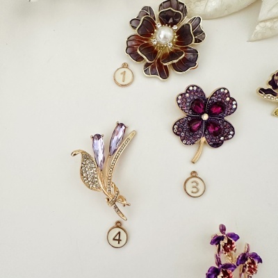 Bijuterias florais em dourado com pedras roxas e pérola, incluindo etiquetas numeradas.