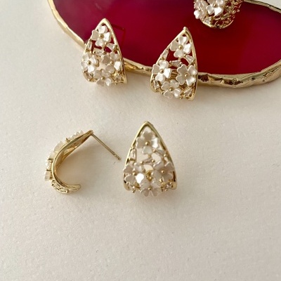 Conjunto de brincos e anel dourados com flores brancas sobre suporte vermelho