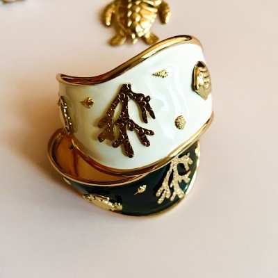 Duas pulseiras largas esmaltadas, uma preta e outra branca, com detalhes dourados e corrente com pendente de tartaruga.