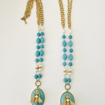 Dois colares dourados com contas azuis e pendentes ovais com abelhas douradas