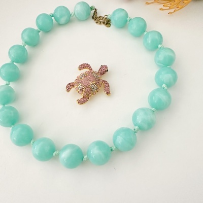 Colar azul com pendente de tartaruga rosa cravejada.