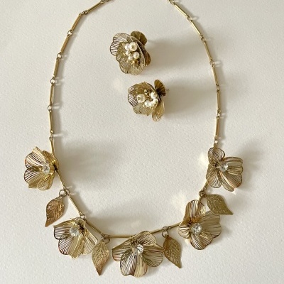 Colar e brincos dourados com flores e folhas detalhadas com cristais.