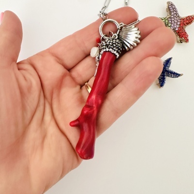 Colar com pendente vermelho em forma de ramo, detalhes prateados e pérola, junto a enfeites estrela do mar coloridos.