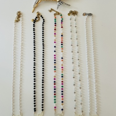 Cinco colares com contas coloridas e pingentes de asas, e um broche de pássaro dourado com detalhes prateados