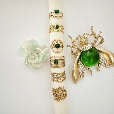 Anéis e broche dourado com pedras verdes e flor decorativa