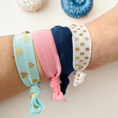 Pulseiras de tecido coloridas com padrões dourados e brincos em forma de caracol ao fundo