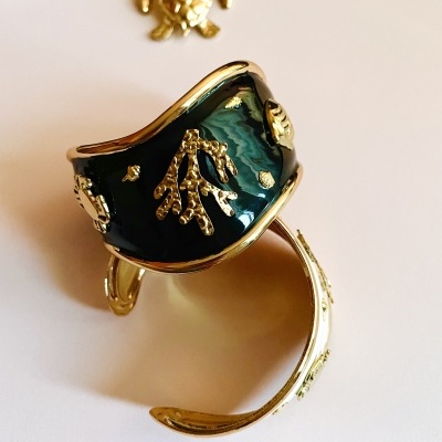 Pulseira dourada com esmalte verde escuro e detalhes em relevo com joias ao fundo