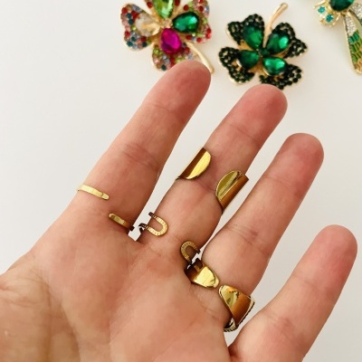 Mão com anéis dourados e broches coloridos ao fundo