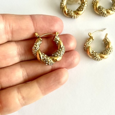 Brincos de argola dourados cravejados com pedras sobre fundo branco