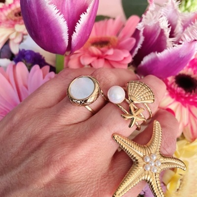 Mão com anéis dourados e pérolas contra fundo de flores coloridas