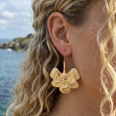 Brinco dourado em forma de flor com textura detalhada e fundo mar