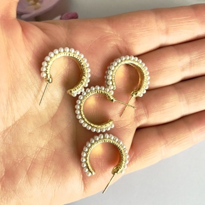 Brincos dourados em forma de argola com pérolas brancas na palma da mão