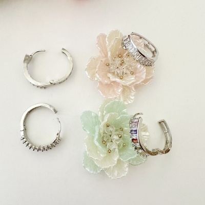 Quatro brincos prateados em argola com pedras sobre flores decorativas rosa pálido e verde claro