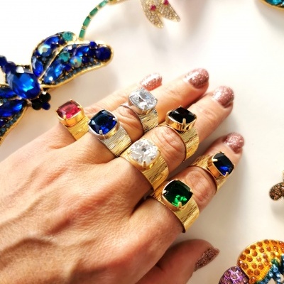 Mão com anéis dourados de pedras coloridas e broches de insetos coloridos no fundo branco